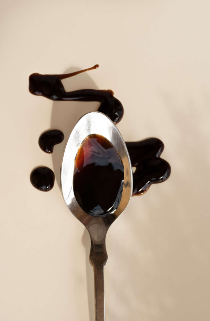 silver spoon with balsamic vinegar , spread onto a beige table